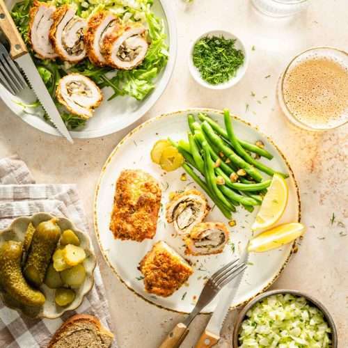 stuffed pork chops served on plates, with green beans, pickles, glass of beer