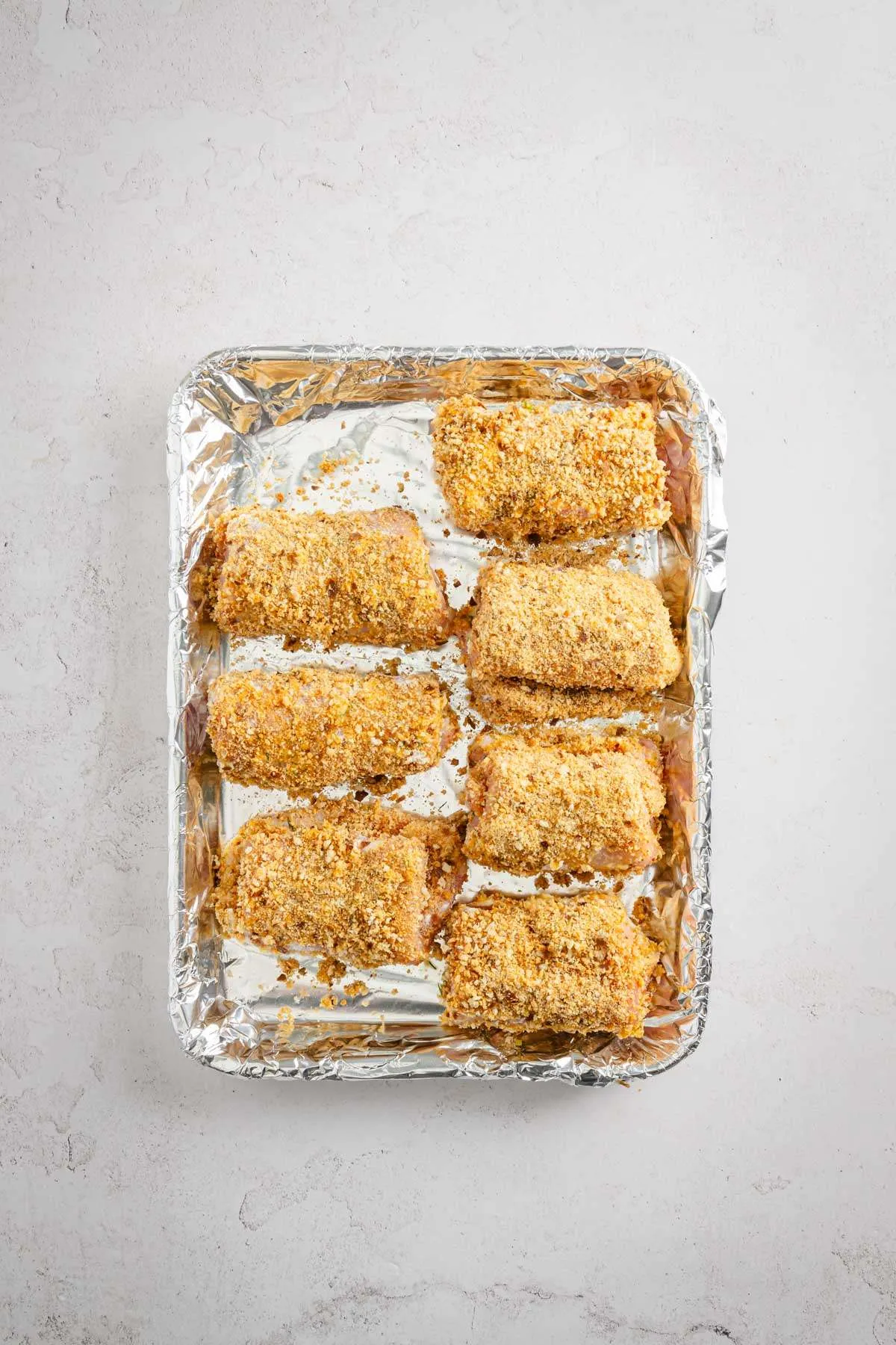 stuffed pork chops ready for frying, on a baking sheet
