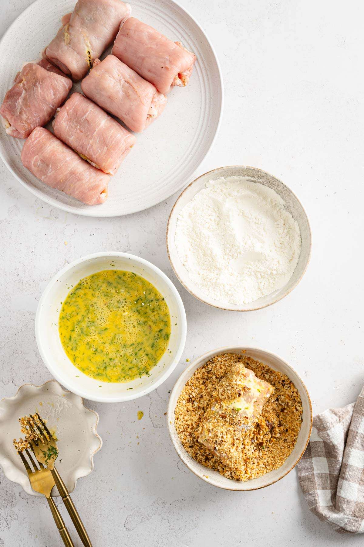 stuffed pork chops ready to be battered, dish with flour, beaten eggs and one with breadcrumbs