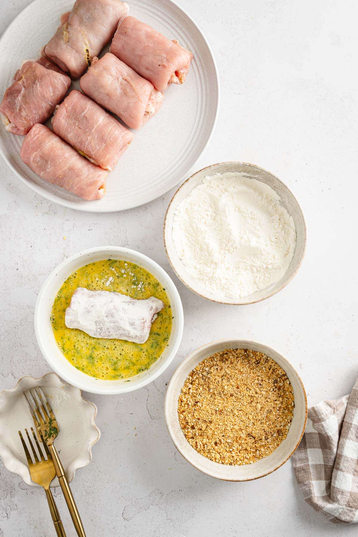 stuffed pork chops ready to be battered, dish with flour, beaten eggs and one with breadcrumbs