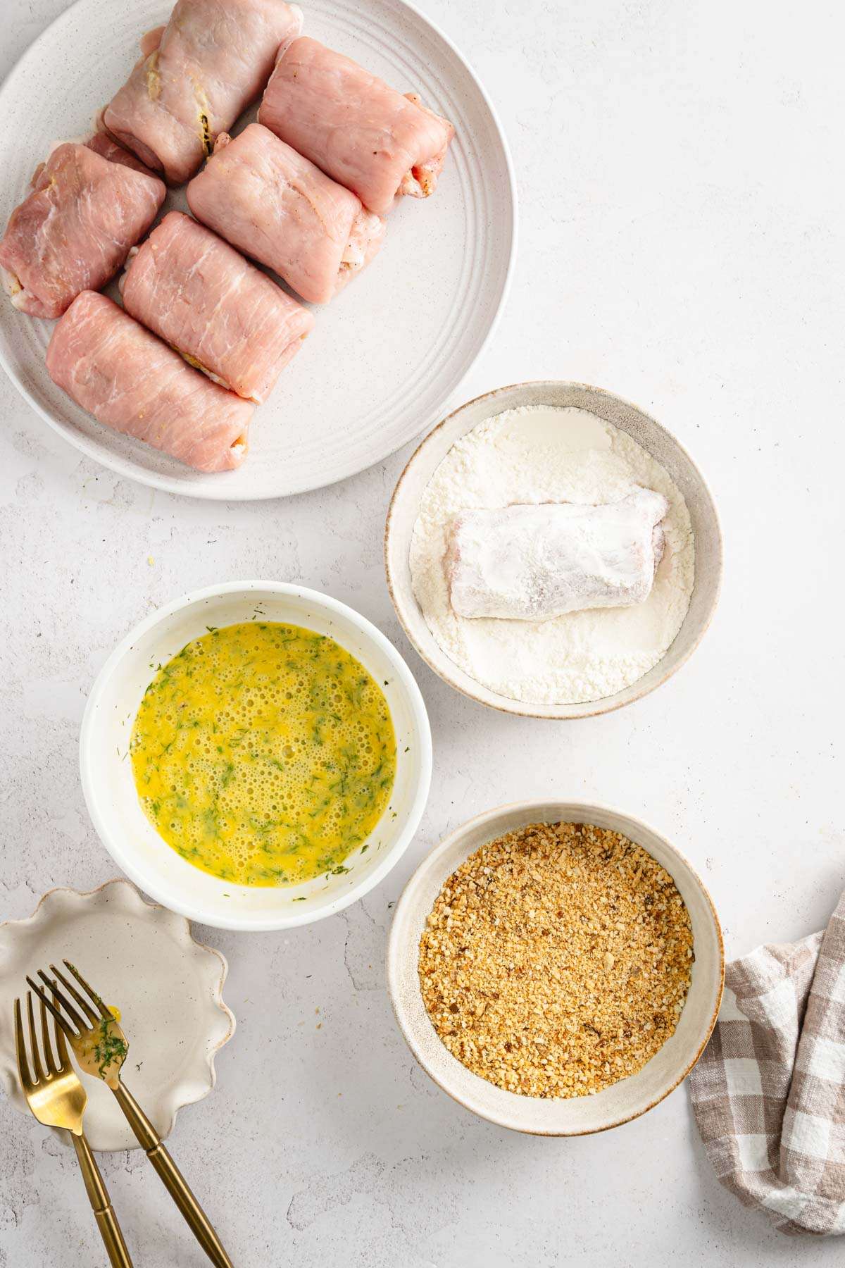 stuffed pork chops ready to be battered, dish with flour, beaten eggs and one with breadcrumbs