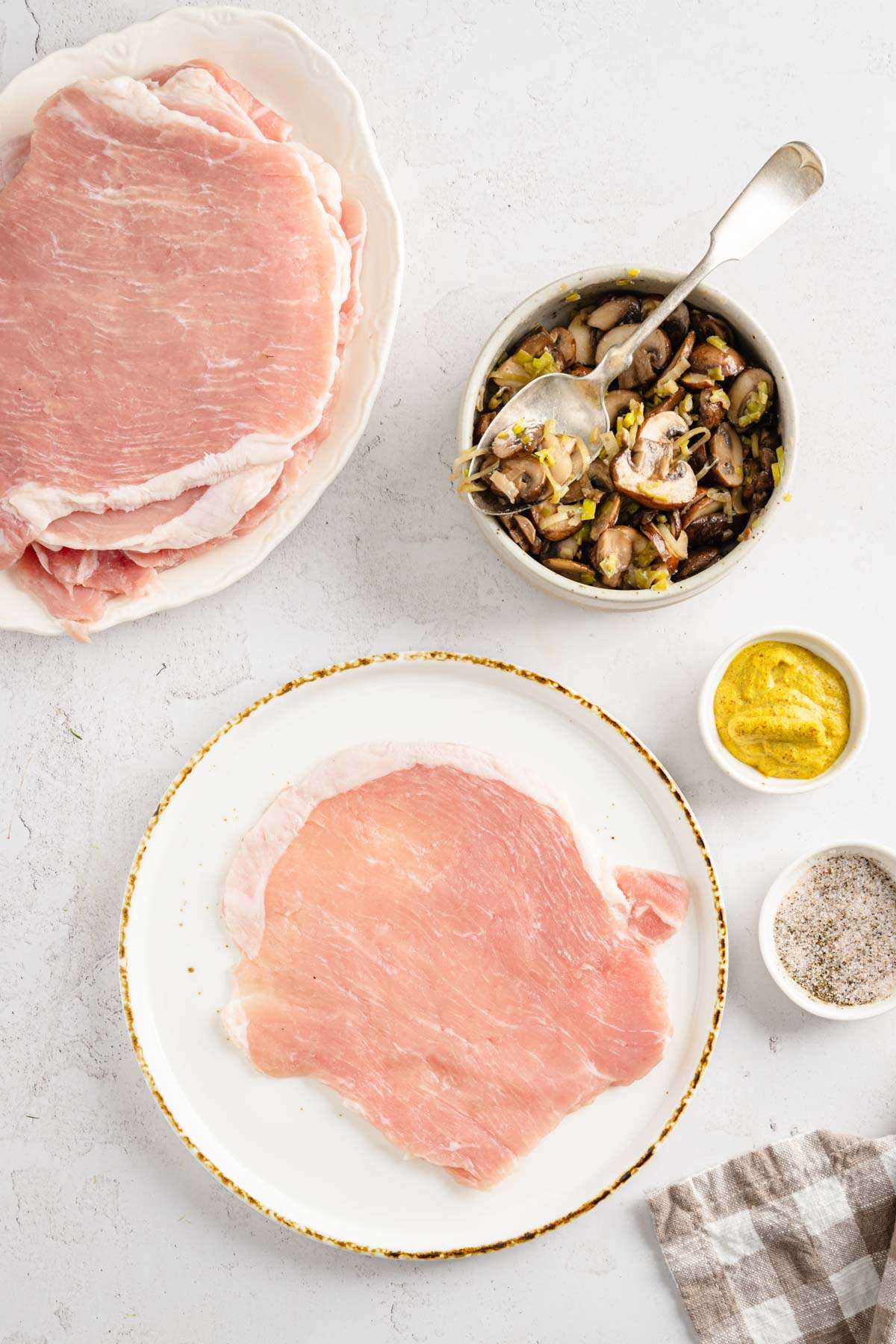 raw por chop on a plate, dish with cooked stuffing, mustard and salt, pepper