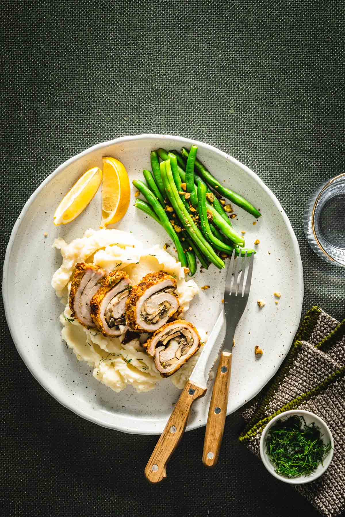 green background, dinner plate with stuffed pork chop cut into slices, green beans, lemon wedges