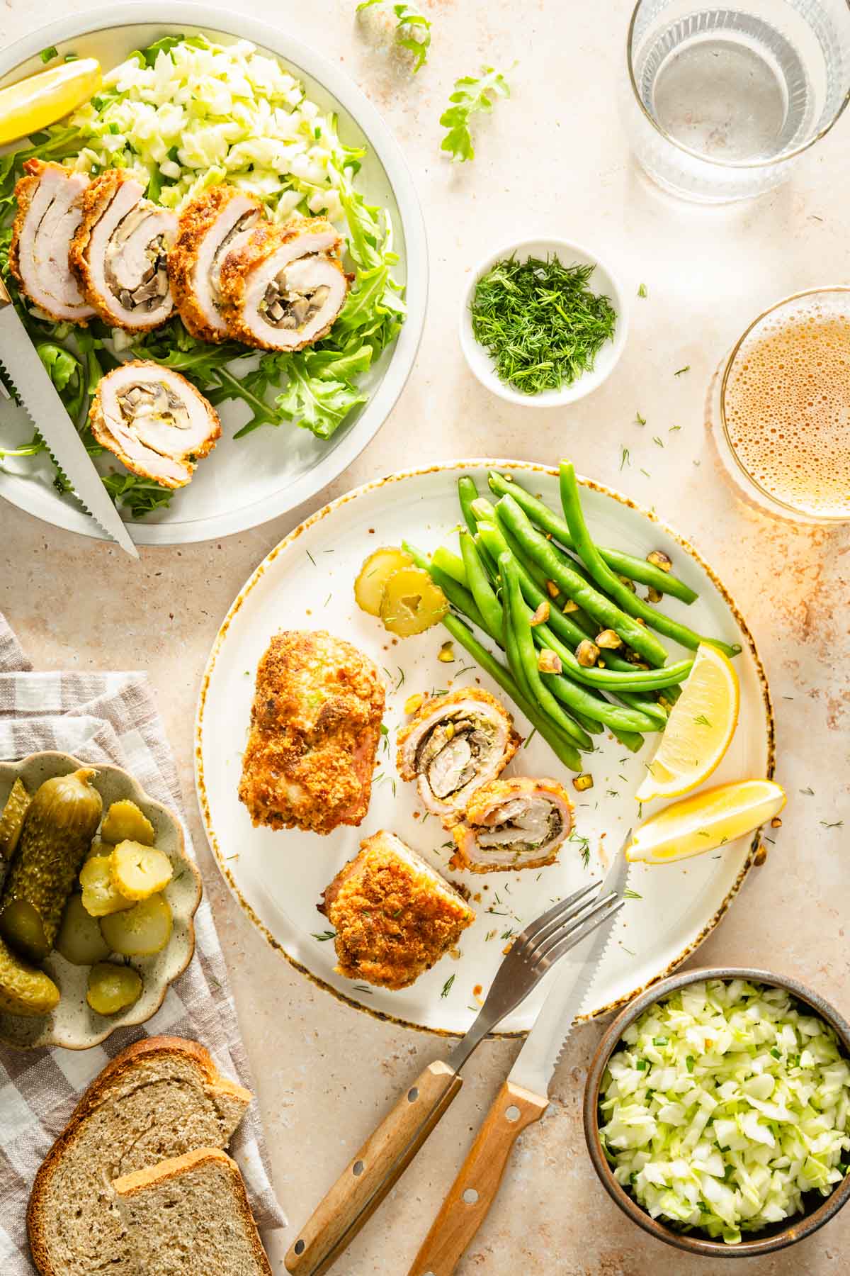 two stuffed pork chops on a plate with green beans, lemon wedges, slices of bread, glass of beer