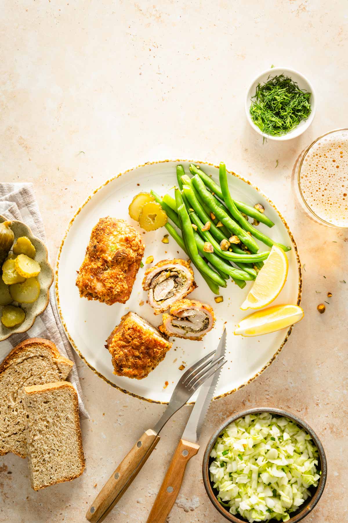 two stuffed pork chops on a plate with green beans, lemon wedges, slices of bread, glass of beer