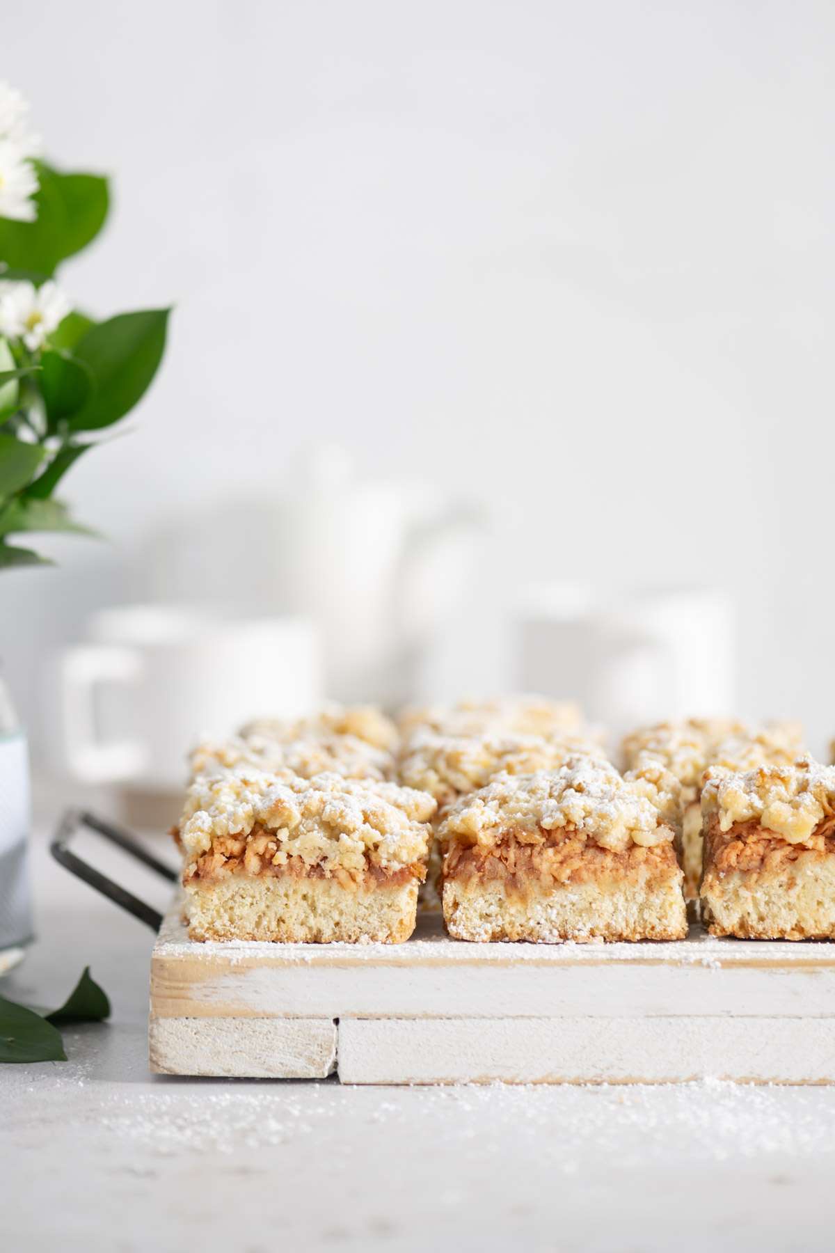 slices of Szarlotka on a serving board, cups and tea kettle in the background