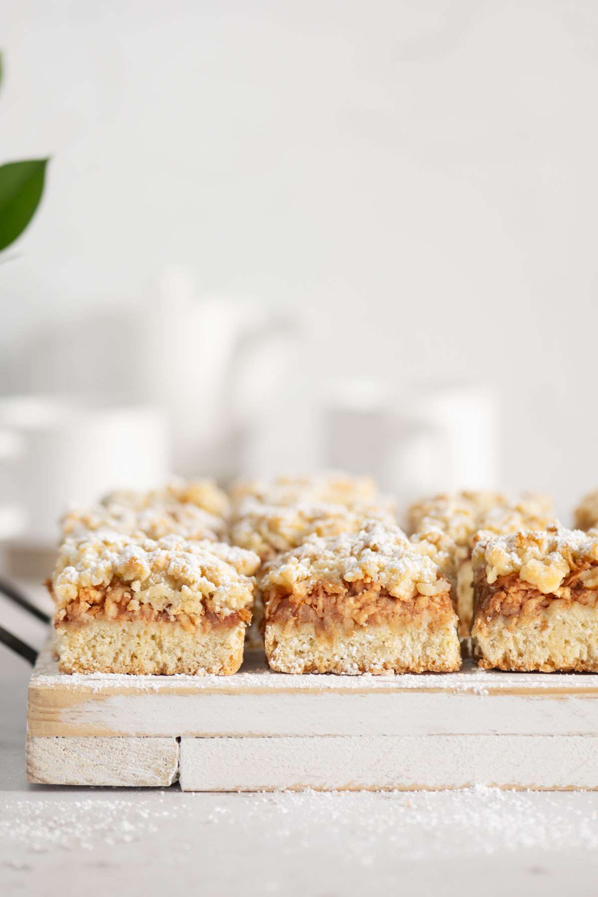 slices of Szarlotka on a serving board, cups and tea kettle in the background