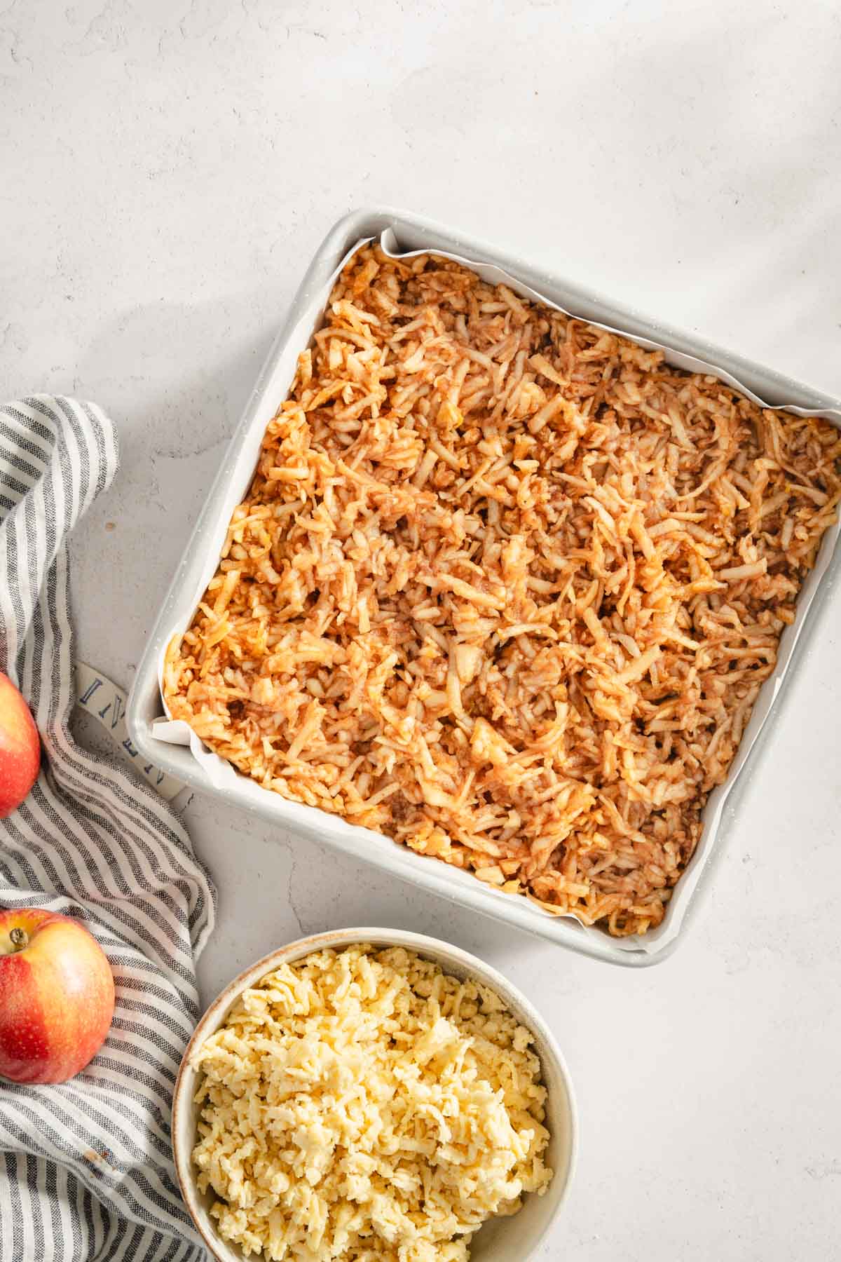 baking pan with dough and shredded apples layered on top, small bowl with shredded dough