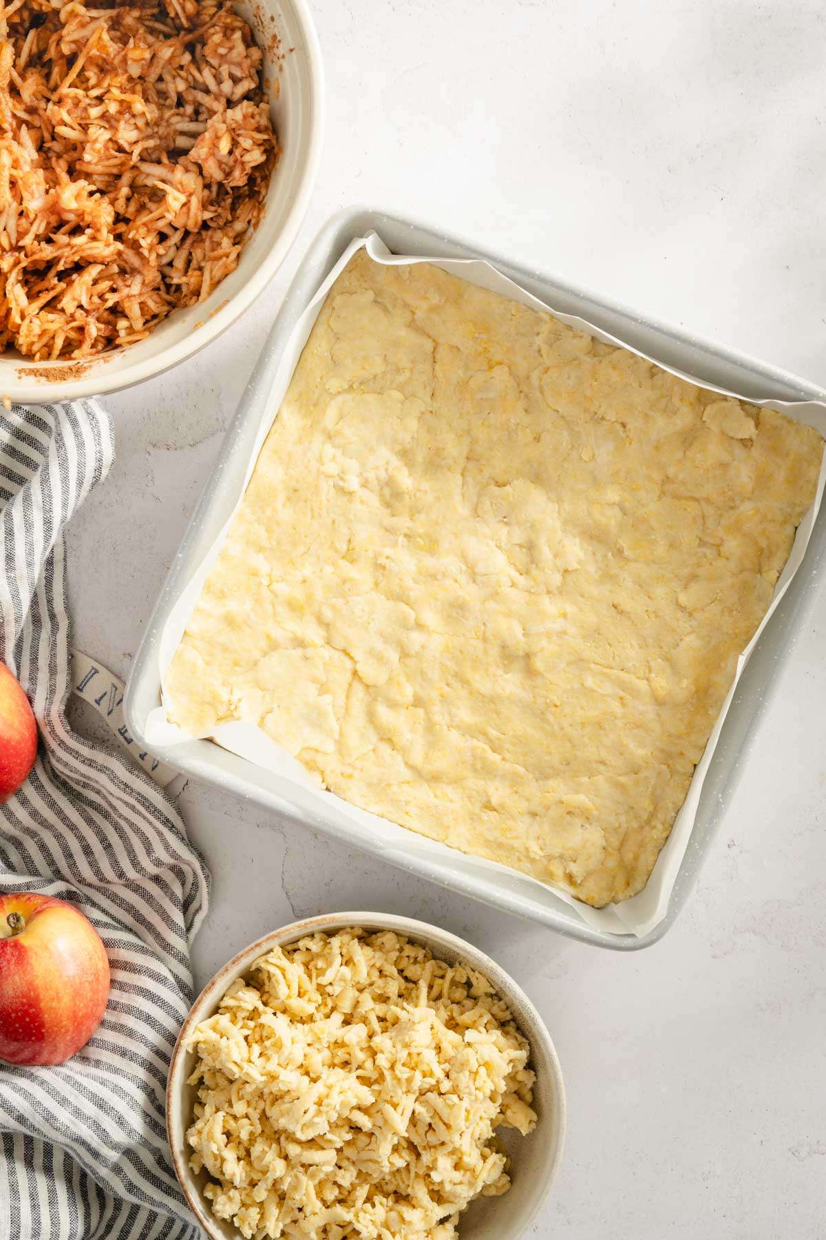 baking dish with dough pressed into it, bowl with shredded apples, bowl with shredded dough