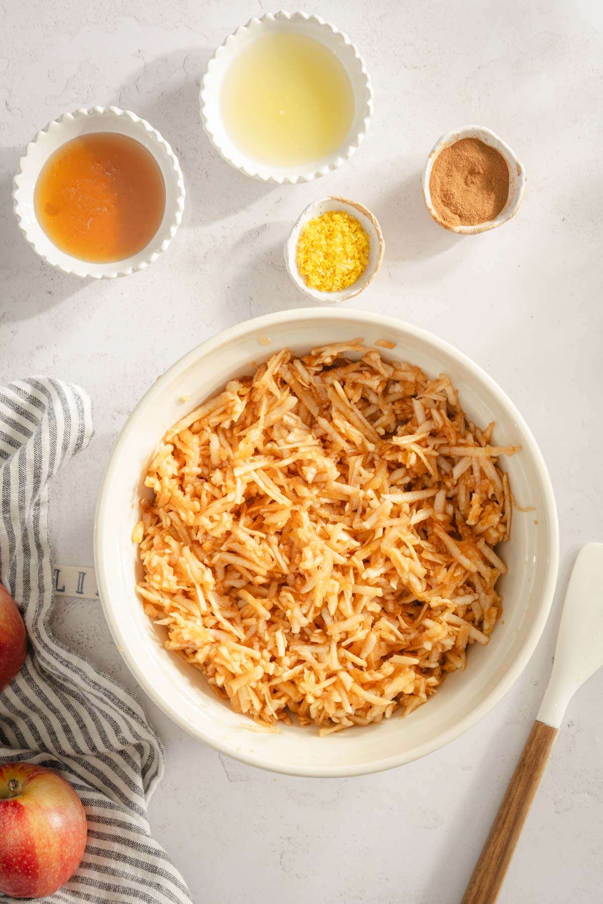 shredded apples in a bowl, small bowls with honey, lemon juice, zest and cinnamon