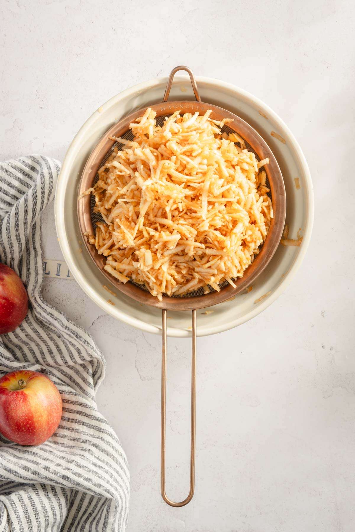 shredded apples in a strainer placed over a bowl