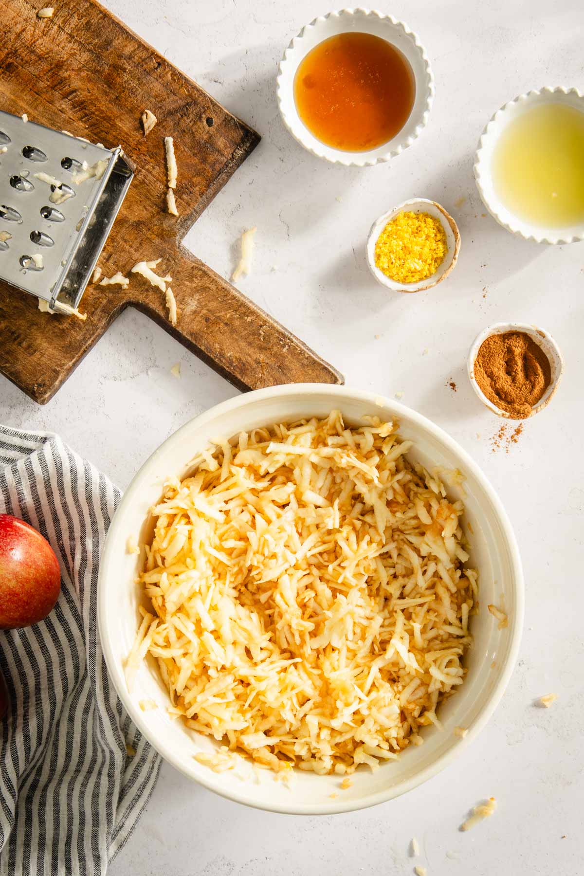 all apples shredded in a bowl, veggie shredded on a cutting board, napkin, small bowls with other ingredients