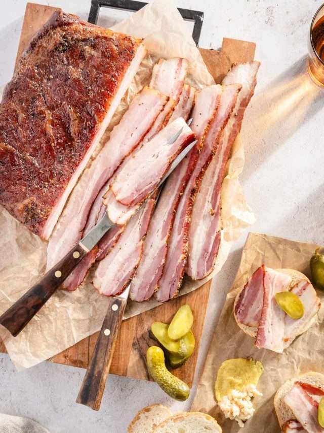 sliced pork belly on a cutting board, few pieces of bread, pickles