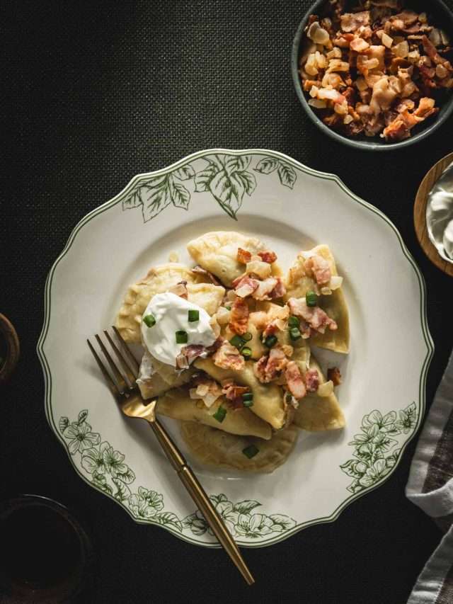 plate with cooked pierogis with bacon-onion topping and a dollop of sour cream