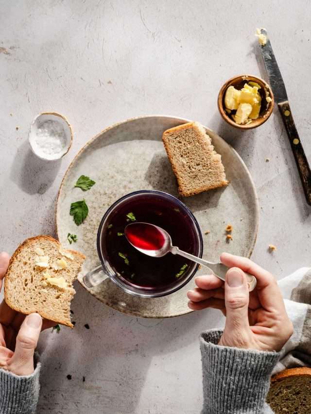 borscht in a mug, hands in frame holding spoon, slices of bread, butter, knife