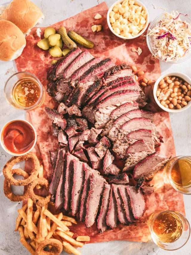 sliced smoked brisket on a butcher paper with different dishes with sides, glasses with beer