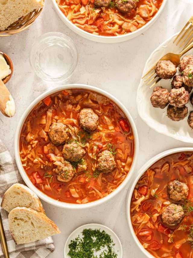 Cabbage soup served in bowls, meatballs on the side, bread knife, bread basket, utensils