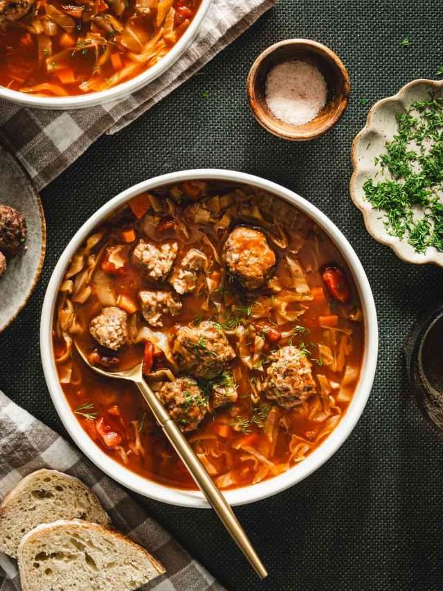 green background, bowl with cabbage soup, meatballs on the plate, dish with fresh dill, napkin, slices of bread, spoon in the soup