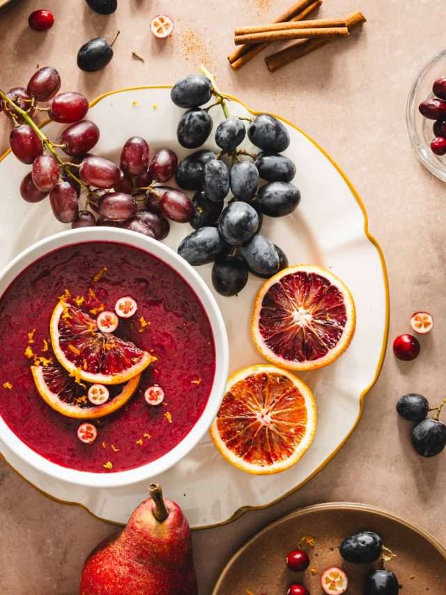 plate with a bowl and cranberry sauce, decorated with orange slices, cut up blood orange, grapes, cinnamon sticks, hole pear, plates with other fruit, close up