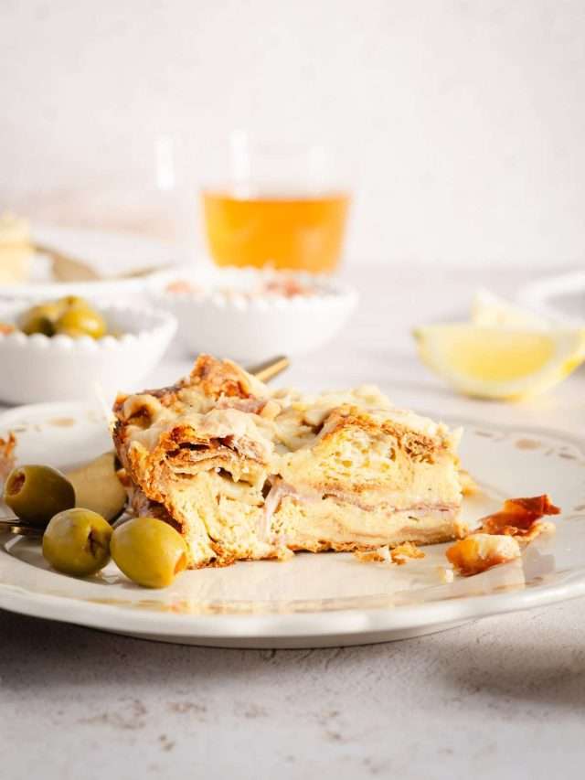 slice of croissant bake on a plate, dishes with olives, sauce, glass with tea