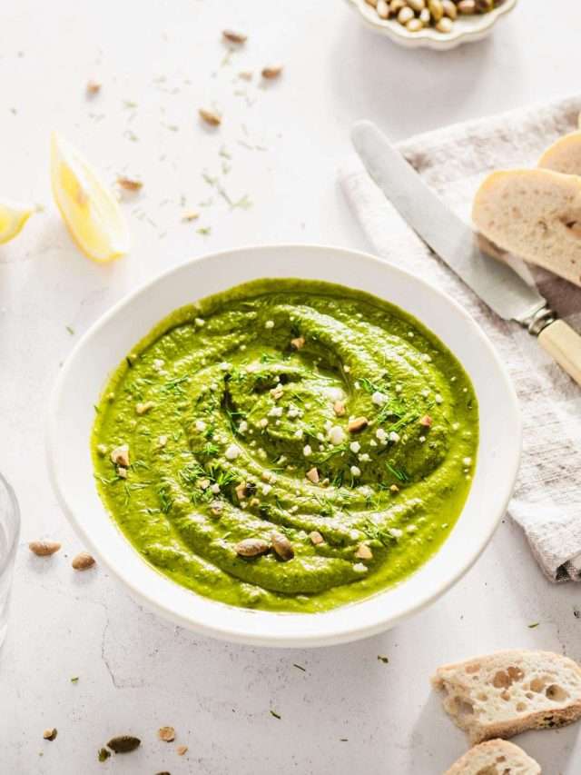 bowl with dill pesto garnished with crushed pumpkin seeds, chopped fresh dill, lemon wedges, bread slices, butter knife, dish with pumpkin seeds