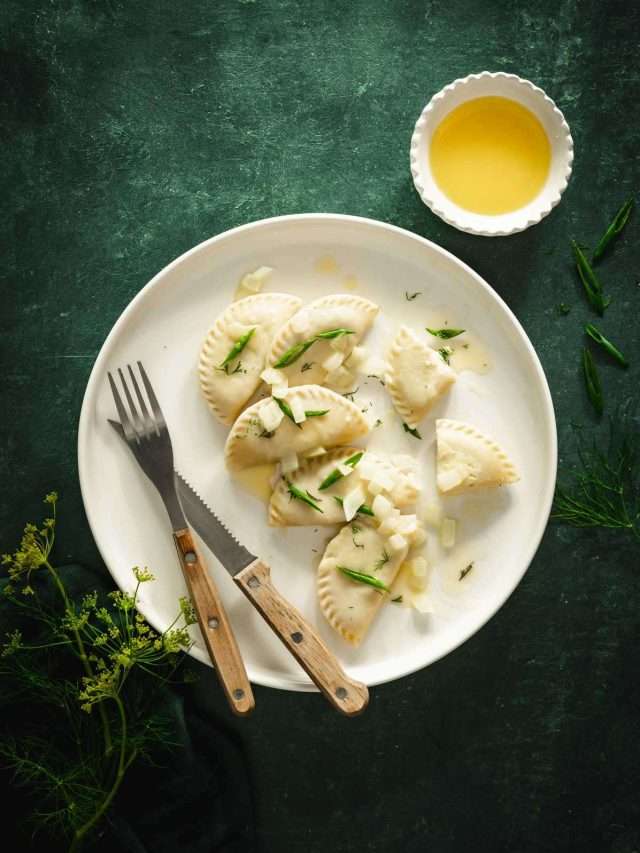 plate with dill pierogis on a dark green background, dish with melted butter, few branches of fresh dill