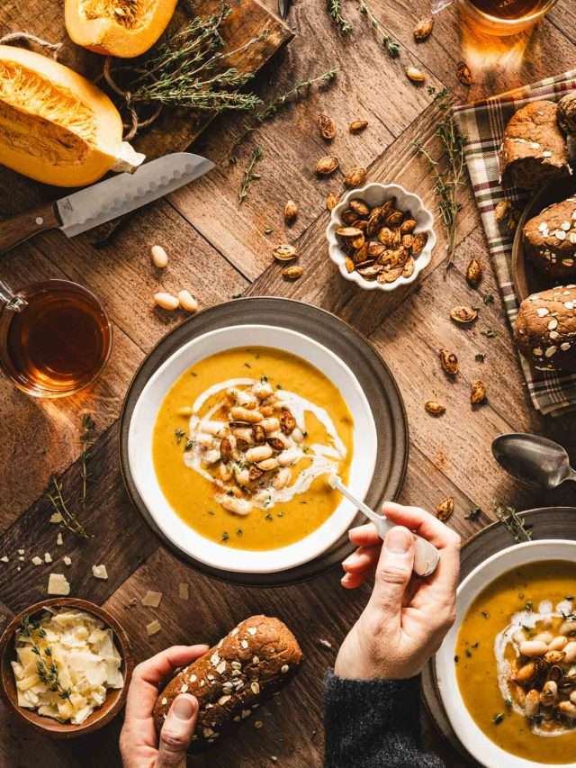 top view of a pumpkin soup in a serving bowl, hands in frame holding spoon