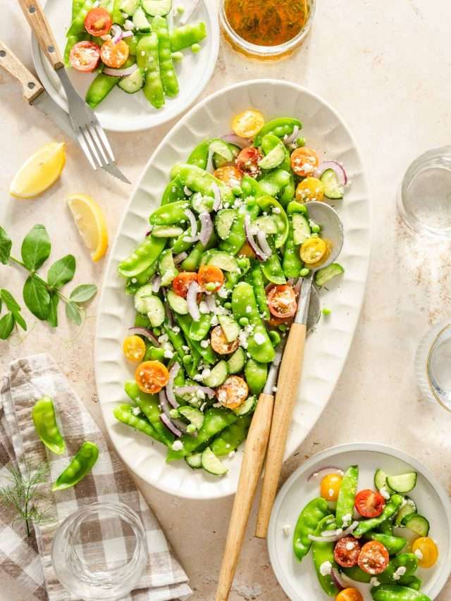 snow pea salad on a serving platter, napkin, serving utensils, few plates with the salad