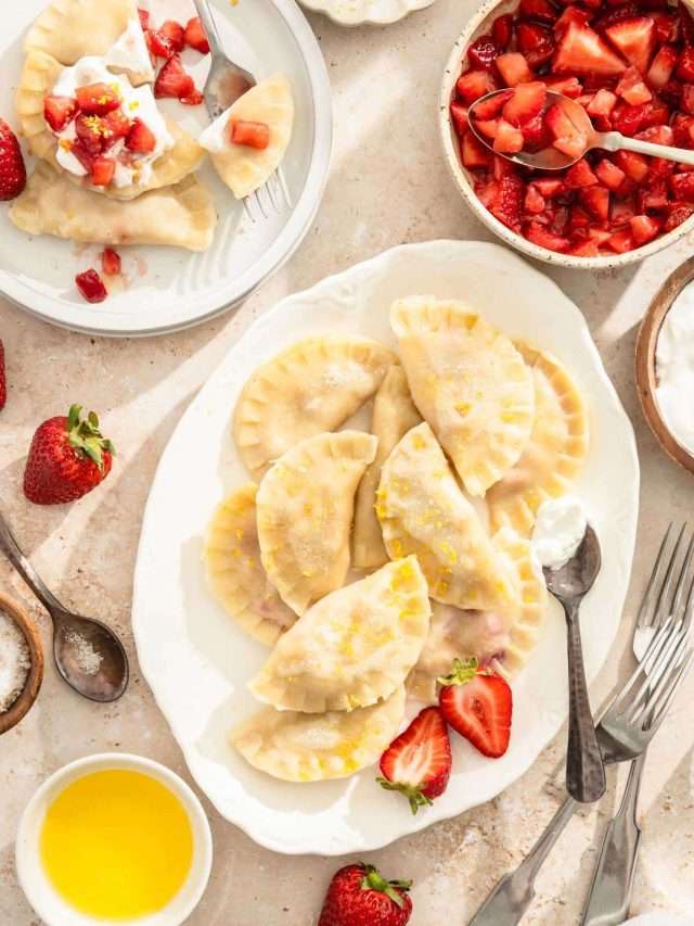 cooked pierogis on a serving platter, plate with few pierogis, small dishes with different toppings, spoons and other utensils