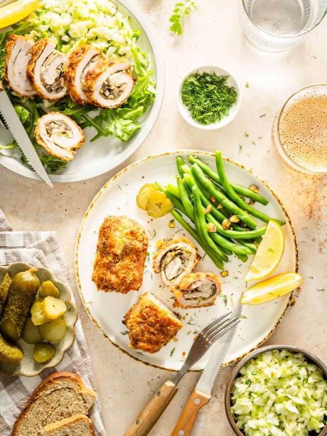 two stuffed pork chops on a plate with green beans, lemon wedges, slices of bread, glass of beer