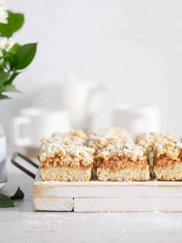 slices of Szarlotka on a serving board, cups and tea kettle in the background