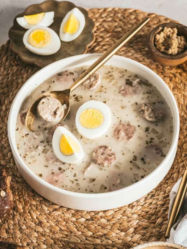 Zurek Soup in a serving bowl with hard boiled egg, piece of bread, small dish with horseradish, spoon, fork, cut up egg on a small plate